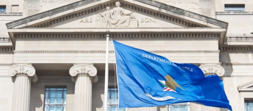 Blue DOJ flag in front of a DOJ building