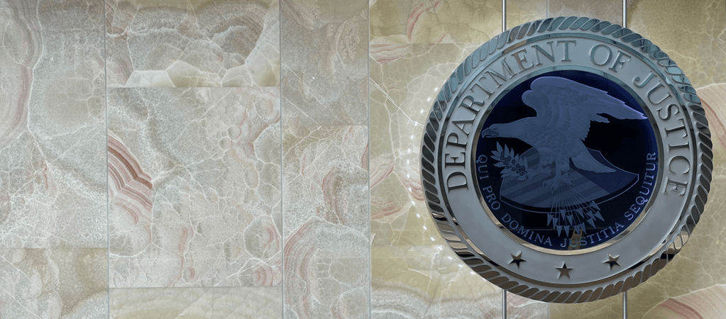 Photo of glass Department of Justice Seal in front of multi-colored wall